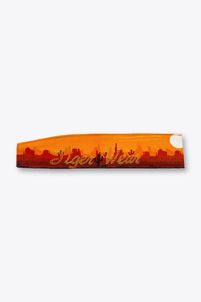 High Noon paintball headband by Tigerwear, laid flat showing the gold rope script over the orange desert sunset print